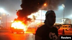 Un supporter de football marche près d'une voiture de police en feu après des affrontements entre les forces de police et des supporters, au Caire, Egypte, le 8 février 2015. 