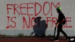 Seorang pengunjuk rasa berjalan melintas di depan grafiti saat unjuk rasa di distrik Sha Tin, pada perayaan Hari Nasional China di Hong Kong, China, 1 Oktober 2019. (Foto: Reuters)