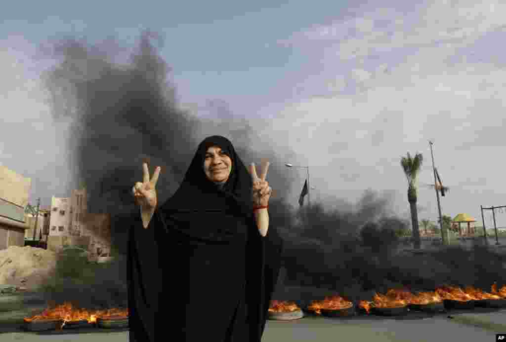 An anti-government protester poses for a photograph flashing the victory sign in front of burning tires on a road in the village of Dumistan, Bahrain, January 7, 2013.