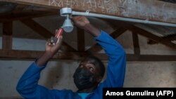 L'étudiant autodidacte Colrerd Nkosi répare une ampoule dans une classe Standard Eight pour éclairer la salle de classe avec de l'électricité générée par la turbine hydroélectrique de Nkosi près du village de Yobe Nkosi, dans le nord du Malawi, le 23 août