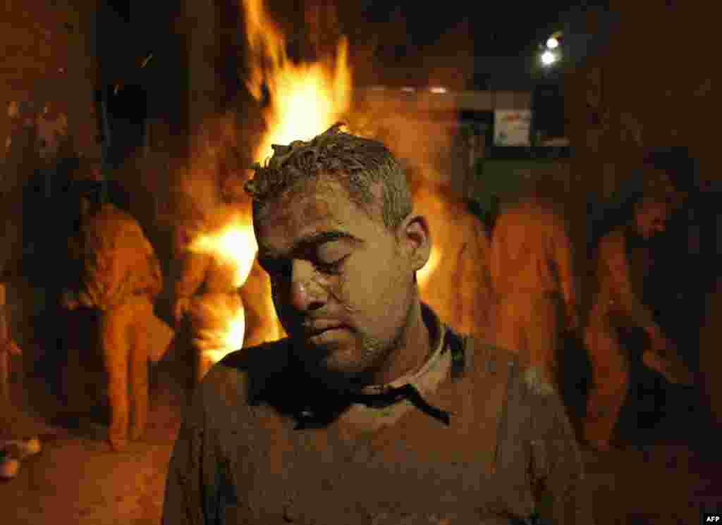 A man covered in mud stands near a fire to dry himself during the Ashura religious festival in Khorramabad, 491 km (305 miles) southwest of Tehran, December 16, 2010. Mourners cover themselves in mud to commemorate the death of Imam Hussein, grandson of t