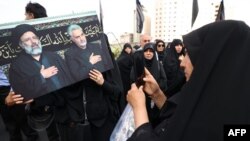 Жінка фотографує плакат, на якому зображено загиблого в аварії гелікоптера президента Ірану Ебрагіма Раїсі й вбитого іранського командувача Касема Сулеймані під час церемонії оплакування у Тегерані, 20 травня 2024 року. (Фото: ATTA KENARE / AFP)