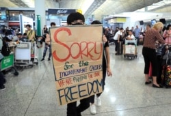 A protester shows a placard to stranded travelers during a demonstration at the Airport in Hong Kong, Aug. 13, 2019.