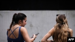 Two women sit on a bench looking at their phone in central Sydney on November 7, 2024.