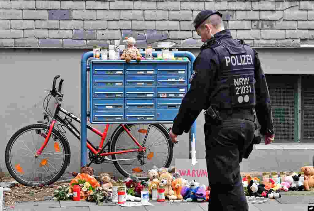 A police officer passes candles and teddy bears at the entrance of a house where five dead children were found in Solingen, Germany. The children&#39;s mother is suspected in the deaths.