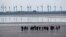 FILE - People explore the wadden sea at the island Norderney, Germany, in front of wind turbines, producing renewable energy, June 1, 2021.