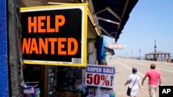 FILE - People walk past a help wanted sign in front of a souvenir shop along the boardwalk, June 2, 2022, in Ocean City, N.J. Different countries have different restrictions on working while attending school as a foreign student.