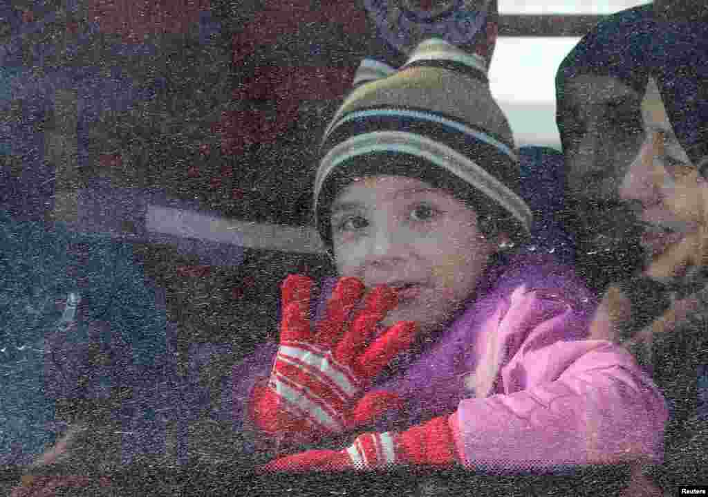 Seorang anak perempuan melambaikan tangan dari dalam bus yang mengevakuasi orang-orang dari Aleppo timur, Suriah (15/12). (Reuters/Abdalrhman Ismail)