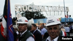 Workers wearing Solidarity safety helmets in front of the shipyard entrance mark the 37th anniversary of emerging Solidarity trade union at the historic shipyard area in Gdansk, Poland, Aug. 31, 2017. Poland lowered the age at which workers can retire, starting Sunday.