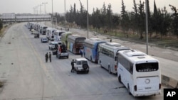 This photo released March, 22, 2108, by the Syrian official news agency SANA, shows Syrian government forces overseeing the evacuation by buses of rebel fighters and their families, at a checkpoint in eastern Ghouta, Syria.