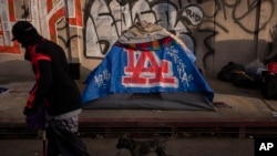 FILE - A man walks past a homeless encampment in downtown Los Angeles, Oct. 25, 2023. 