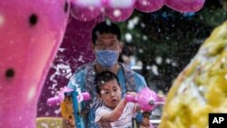 A man wearing a mask to curb the spread of the new coronavirus and a child, who temporarily removed his, enjoy a ride at a local park in Beijing, China, May 23, 2020. 