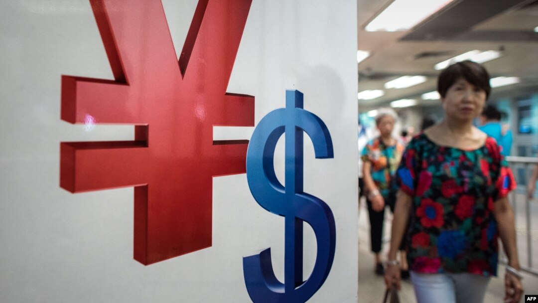 A woman walks past a yuan, left, and a U.S. dollar, right, currency sign in Hong Kong, Aug. 13, 2015.