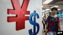 A woman walks past a yuan (L) and a US dollar (R) currency sign in Hong Kong on Aug. 13, 2015.