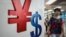 A woman walks past a yuan, left, and a U.S. dollar, right, currency sign in Hong Kong, Aug. 13, 2015.
