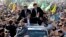 Escorted by his bodyguards, Iranian President Mahmoud Ahmadinejad, center, waves to well wishers from his car, during an annual rally commemorating the anniversary of the 1979 Islamic revolution, which toppled the late pro-U.S. Shah, Mohammad Reza Pahlavi