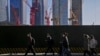 FILE - People wearing face masks walk by construction cranes near office buildings at the central business district in Beijing on March 15, 2023. 