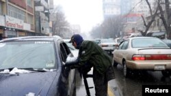 FILE - A Taliban member searches a car as he stands guard at a checkpoint during a snowfall in Kabul, Afghanistan, Jan. 3, 2022. 