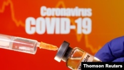 FILE PHOTO: A small bottle labeled with a "Vaccine" sticker is held near a medical syringe in front of displayed "Coronavirus COVID-19" words in this illustration