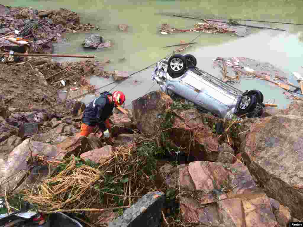 A rescue worker is seen next to an overturned car at the site of a landslide caused by heavy rains from Typhoon Megi, in Sucun Village, Lishui, Zhejiang province, China.