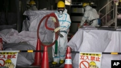 In this Feb. 12, 2020, photo, a worker in a hazmat suit carries a hose while working at a water treatment facility at the Fukushima Dai-ichi nuclear power plant in Okuma, Fukushima Prefecture, Japan. 
