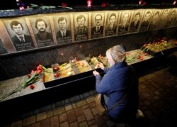 A woman wearing a protective mask lights a candle at a memorial, dedicated to firefighters and workers who died after the Chernobyl nuclear disaster, during a night service in Slavutych, Ukraine, April 26, 2020.