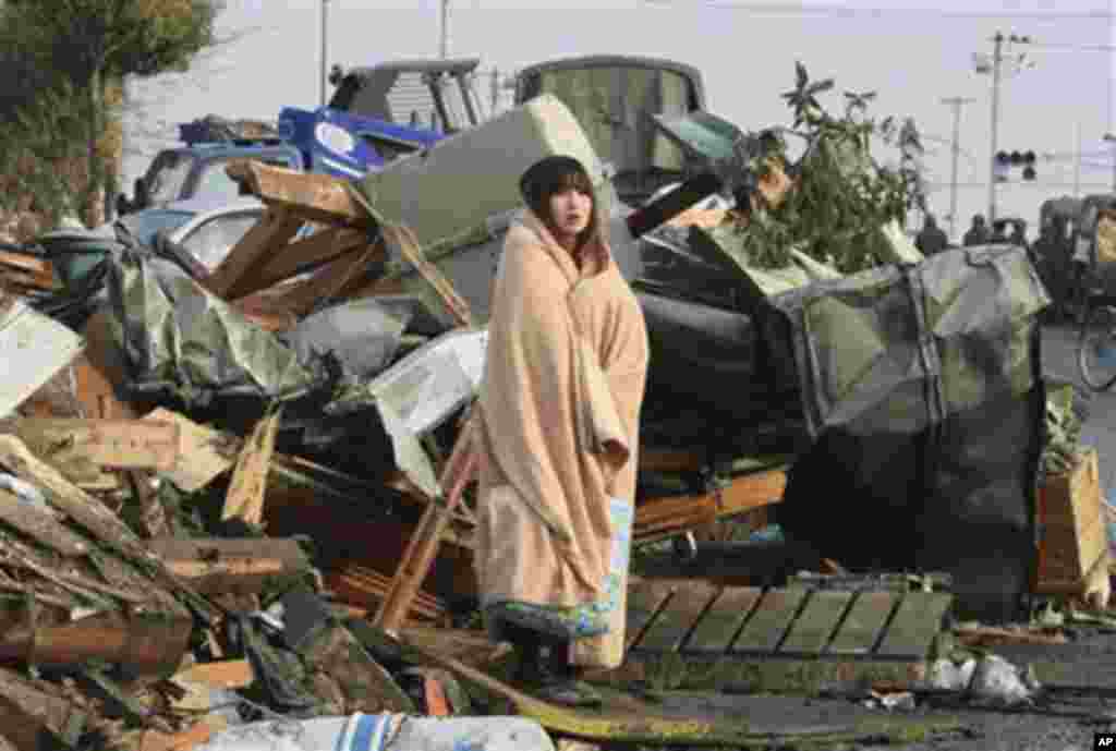 A woman wrapped up in a blanket stands in the middle of rubble, looking at the city submerged under water in Ishinomaki in Miyagi Prefecture (state) Sunday morning, March 13, 2011.