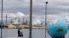 FILE - People walk past an Earth globe sculpture at Thea's Park in Tacoma, Washington, with the WestRock Paper Mill in the background, April 21, 2020.