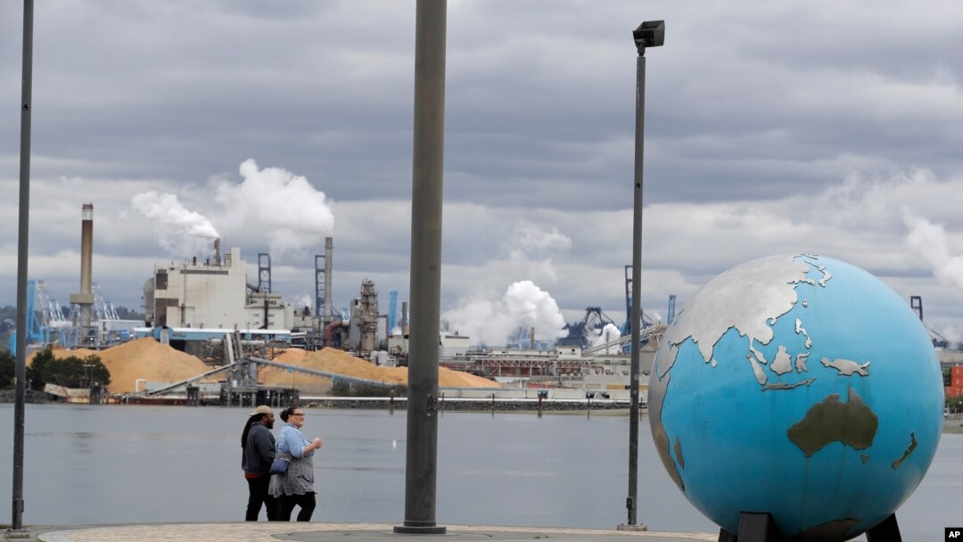 FILE - People walk past an Earth globe sculpture at Thea's Park in Tacoma, Washington, with the WestRock Paper Mill in the background, April 21, 2020.