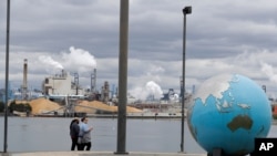 FILE - People walk past an Earth globe sculpture at Thea's Park in Tacoma, Washington, with the WestRock Paper Mill in the background, April 21, 2020.