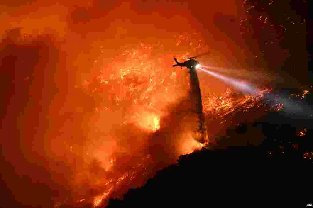 A fire fighting helicopter drops water as the Palisades fire grows near the Mandeville Canyon neighborhood and Encino, California, Jan. 11, 2025.&nbsp;The Palisades Fire, the largest of the Los Angeles fires, spread toward previously untouched neighborhoods, forcing new evacuations and dimming hopes that the disaster was coming under control.