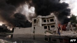 An Iraqi man walks near smoke billowing from oil wells, set ablaze by Islamic State (IS) group militants before fleeing the oil-producing region of Qayyarah, Aug. 30, 2016.