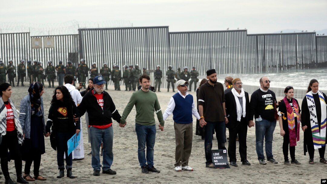 Orang-orang bergandengan tangan seraya berdoa saat berunjuk rasa di San Diego, dekat perbatasan dengan Tijuana, Meksiko, 10 Desember 2018 (foto: AP Photo/Gregory Bull)