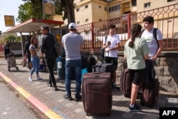 FILE - People with their luggage wait at a bus stop in the northern Israeli town of Kiryat Shmona on the border with Lebanon, to be evacuated to a safer location on October 22, 2023.