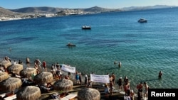 ชาวกรีซถือป้ายประท้วงที่เกาะแพรอส (ที่มา: รอยเตอร์)