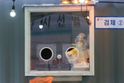 FILE - A medical worker in a booth sprays disinfectant as she waits for people to come for tests at a coronavirus testing site in Seoul, South Korea, Feb. 5, 2021.