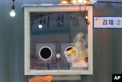 FILE - A medical worker in a booth sprays disinfectant as she waits for people to come for tests at a coronavirus testing site in Seoul, South Korea, Feb. 5, 2021.