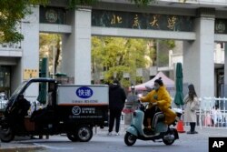 A woman wearing mask rides past an entrance to Peking University in Beijing, Wednesday, Nov. 16, 2022.