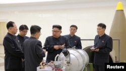 En esta foto publicada por la agencia estatal de noticias de Corea del Norte, el líder Kim Jong Un, conversa con los desarrolladores de armas nucleares sobre uno de los armamentos en que trabajaban en 2017.