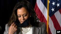 FILE - Democratic vice presidential candidate Senator Kamala Harris, then still the nominee, removes her face mask as she prepares to speak at the Hotel DuPont in Wilmington, Delaware, Aug. 13, 2020. 