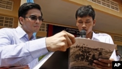 Dy Khamboly, left, a staff member at the Documentation Center of Cambodia, helps a student read his book "A History of Democratic Kampuchea" in Anlong Veng, in Oddar Meanchey province. 