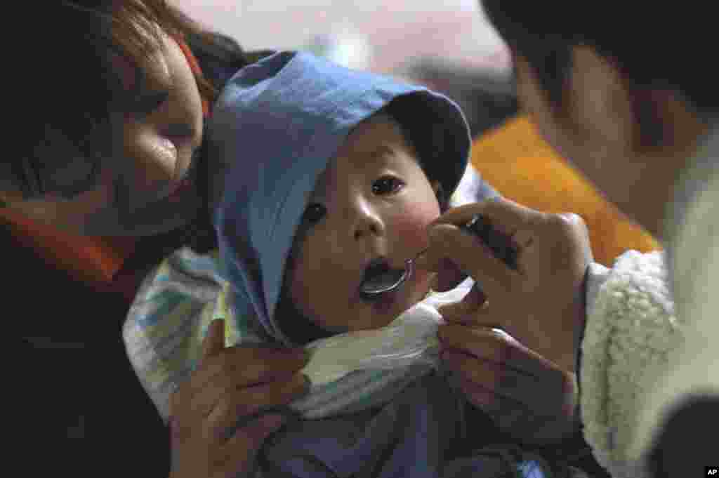 A woman (L) holds her baby as her relative feeds him at a shelter for survivors at a village that was destroyed by an earthquake and tsunami in Yamada, northeast Japan March 17, 2011.  REUTERS/Lee Jae-Won