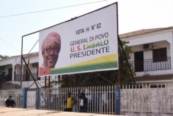 Two men stand in front of a sign of opposition Presidential candidate Umaro Sissoco Embalo in Bissau, Dec. 27, 2019.