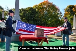 Civil War re-enactors fold an American flag near an urn, center, containing the cremated remains of Byron R. Johnson, a Union soldier who fought in the Civil War, during funeral services, Oct. 16, 2024, at Oak Grove Cemetery in Pawtucket, Rhode Island.