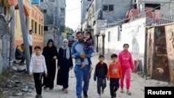 Sejumlah warga Palestina tampak berjalan kembali ke rumah mereka yang hancur selama pertempuran antara pasukan Israel dan militan Palestina, di Deir Al-Balah, Gaza, pada 14 Mei 2023. (Foto: Reuters/Ibraheem Abu Mustafa)