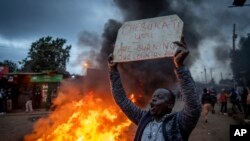 A supporter of presidential candidate Raila Odinga holds a placard referring to electoral commission chairman Wafula Chebukati, next to a roadblock of burning tires in the Kibera neighborhood of Nairobi, Kenya Monday, Aug. 15, 2022.