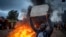 A supporter of presidential candidate Raila Odinga holds a placard referring to electoral commission chairman Wafula Chebukati, next to a roadblock of burning tires in the Kibera neighborhood of Nairobi, Kenya Monday, Aug. 15, 2022.