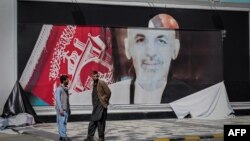 Dy burra afganë qëndrojnë përpara një posteri të grisur të Presidentit afgan Ashraf Ghani (16 gusht 2021)