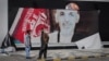 FILE - Afghan men stand next to a torn poster of deposed Afghan President Ashraf Ghani at Kabul airport, Aug. 16, 2021.