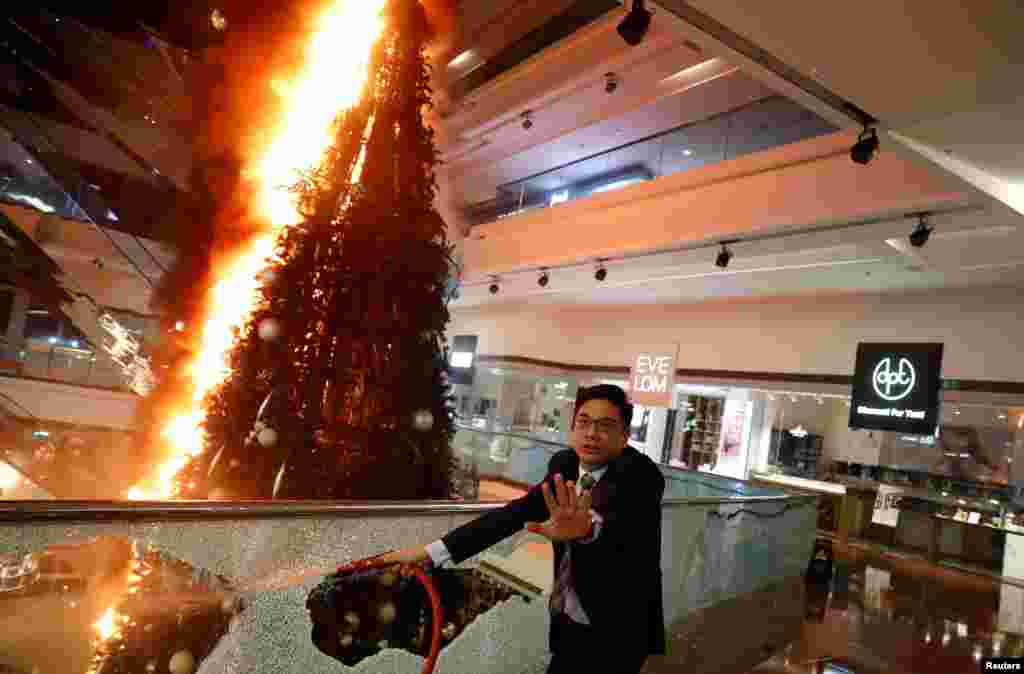 A man reacts as he tries to extinguish a burning Christmas tree at the Festival Walk Mall in Kowloon Tong, Hong Kong, China. Anti-government protesters smashed windows and set fires in the mall, including the Christmas tree.